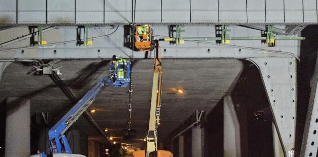 Nighttime construction work under a bridge with elevated platforms and workers.