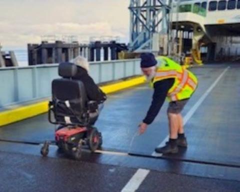 A person in a wheelchair is guided onto a ferry by someone in a high-visibility vest