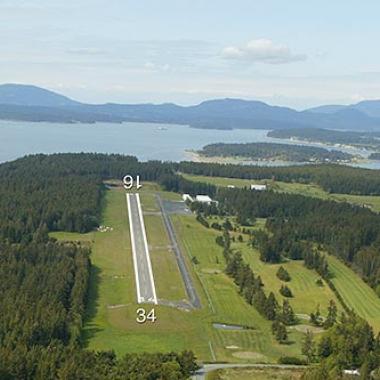 Lopez Airport runway located around trees and near a body of water.