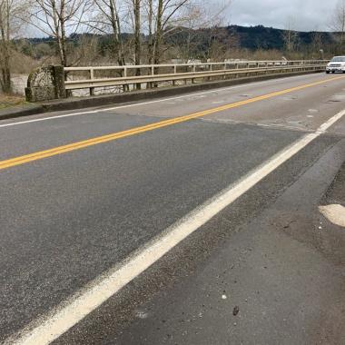 Two cars drive over a bridge with visible potholes