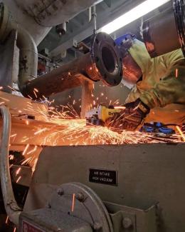 Worker grinding metal, producing bright orange sparks in an industrial setting